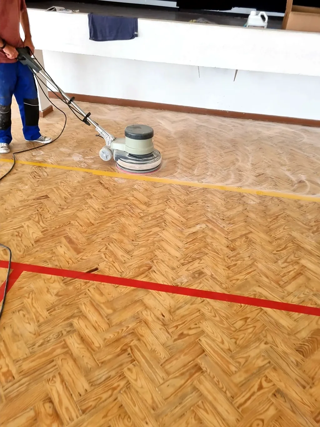 Polimento de um piso de parquet em espinha num pavilhão, com a máquina de polir